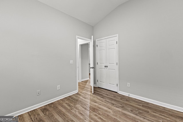 unfurnished bedroom featuring vaulted ceiling, baseboards, and wood finished floors