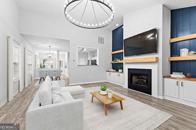 living area featuring an inviting chandelier, visible vents, light wood finished floors, and high vaulted ceiling