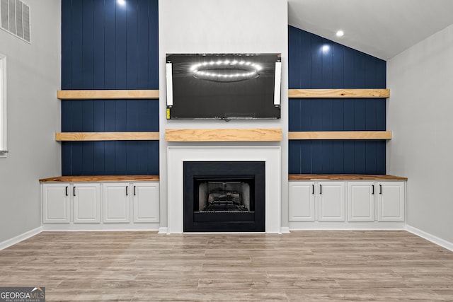 unfurnished living room featuring a fireplace, lofted ceiling, visible vents, wood finished floors, and baseboards