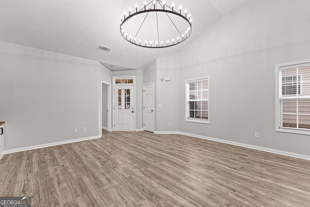 unfurnished living room with baseboards, visible vents, wood finished floors, an inviting chandelier, and high vaulted ceiling