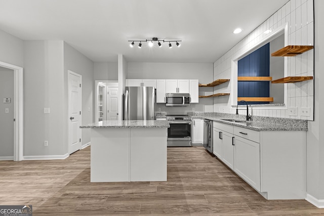 kitchen with a kitchen island, stainless steel appliances, white cabinetry, open shelves, and a sink