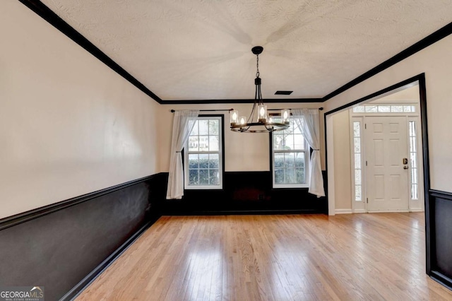 unfurnished dining area with a textured ceiling, ornamental molding, and wood finished floors