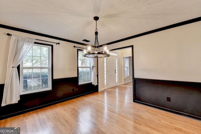 unfurnished dining area featuring baseboards, visible vents, wood finished floors, crown molding, and a chandelier