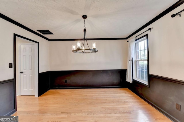 unfurnished dining area with light wood-type flooring, a chandelier, crown molding, and wainscoting