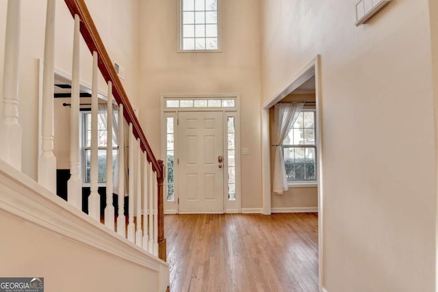 entryway with stairway, wood finished floors, a towering ceiling, and baseboards