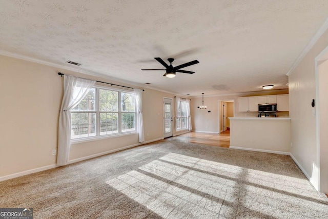 unfurnished living room featuring crown molding, light colored carpet, visible vents, a textured ceiling, and baseboards