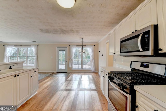 kitchen featuring crown molding, light countertops, appliances with stainless steel finishes, light wood-style floors, and a sink