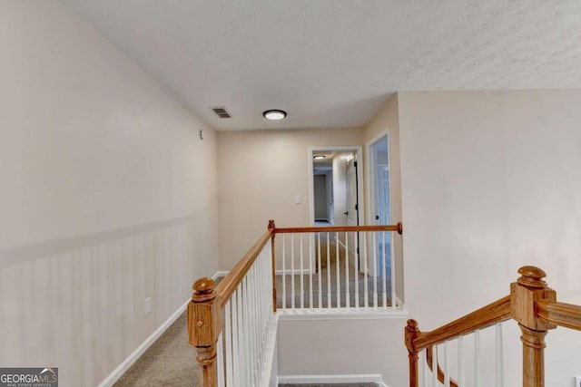 corridor with baseboards, visible vents, a textured ceiling, an upstairs landing, and carpet floors