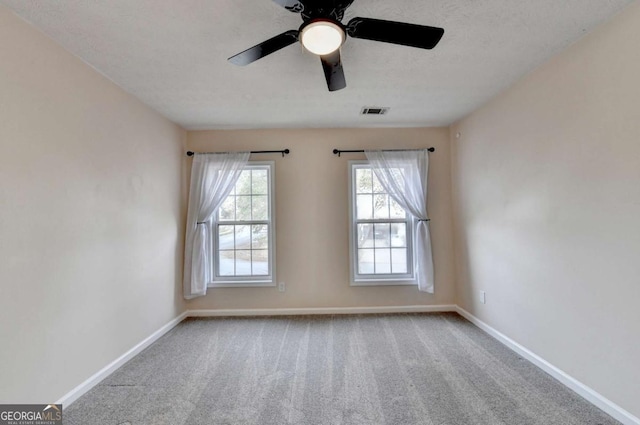 carpeted spare room featuring a textured ceiling, a ceiling fan, visible vents, and baseboards