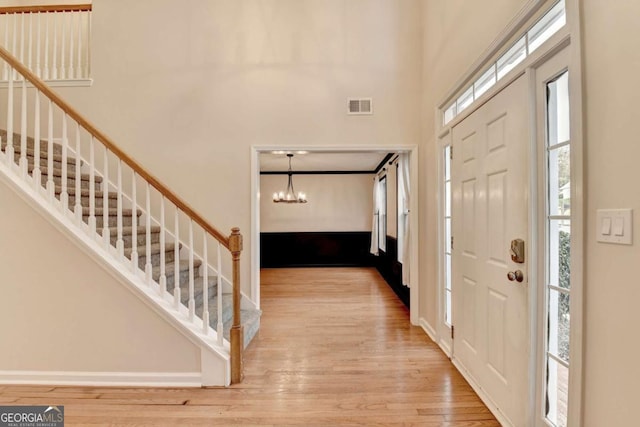 foyer featuring a high ceiling, wood finished floors, visible vents, stairs, and an inviting chandelier