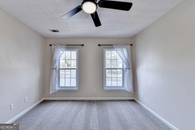 carpeted empty room featuring a ceiling fan, visible vents, a textured ceiling, and baseboards