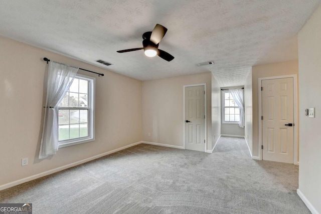 carpeted empty room featuring baseboards, visible vents, ceiling fan, and a textured ceiling