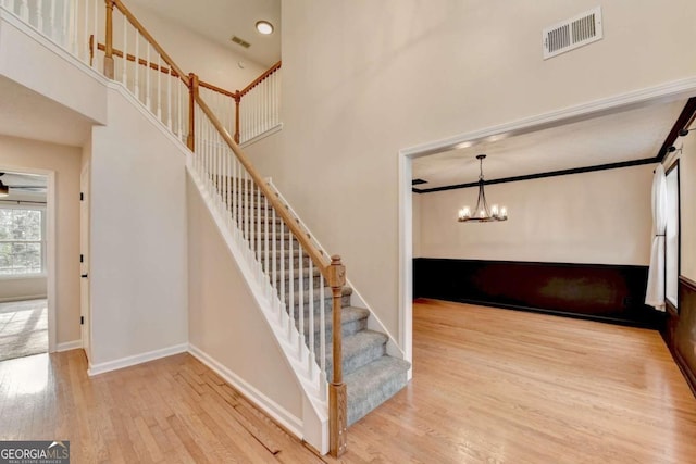 stairs featuring a high ceiling, wood finished floors, visible vents, and baseboards