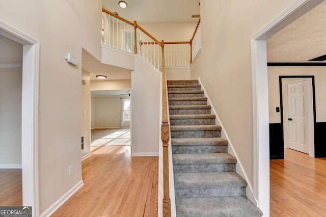 staircase with crown molding, a towering ceiling, baseboards, and wood finished floors