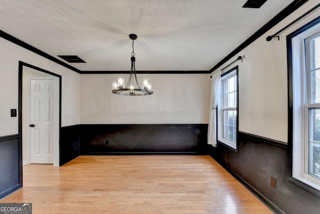 unfurnished dining area with visible vents, a wainscoted wall, a textured ceiling, crown molding, and light wood-style floors