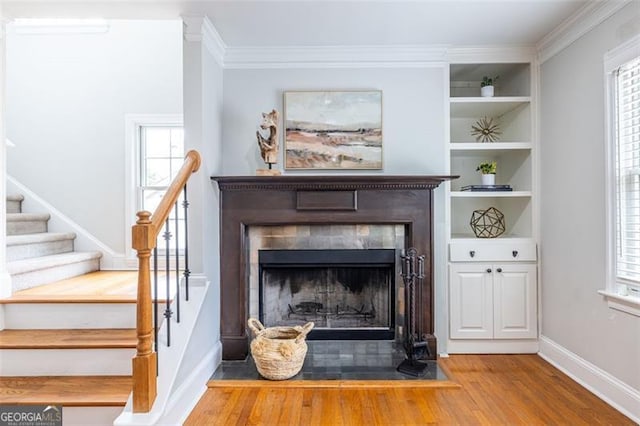 room details with built in shelves, a fireplace with flush hearth, wood finished floors, baseboards, and ornamental molding