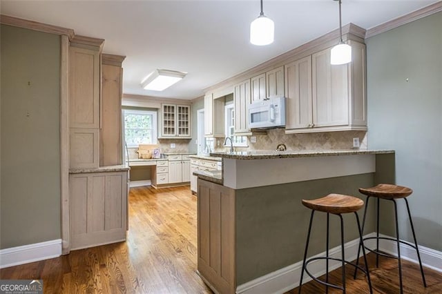 kitchen with a peninsula, white microwave, light stone counters, and decorative backsplash