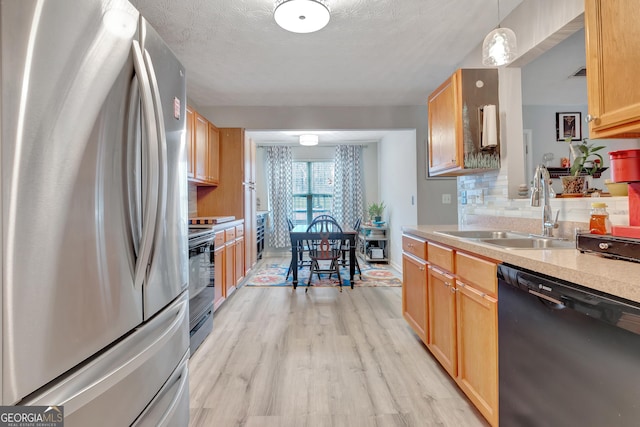 kitchen featuring light wood finished floors, tasteful backsplash, light countertops, black appliances, and a sink