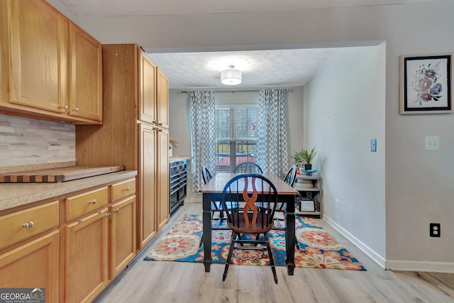 dining space featuring light wood finished floors, baseboards, and a textured ceiling