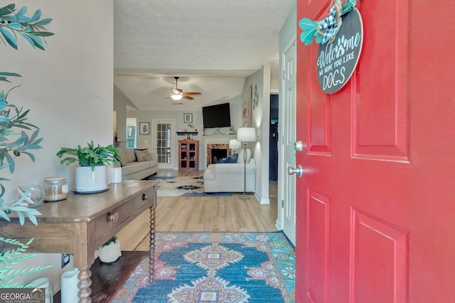 foyer entrance with a textured ceiling, ceiling fan, a fireplace, and wood finished floors