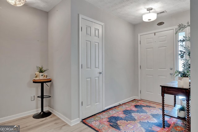 entrance foyer with visible vents, a textured ceiling, baseboards, and wood finished floors