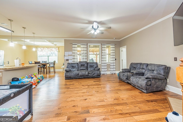 living room with light wood-style floors, ornamental molding, baseboards, and a ceiling fan