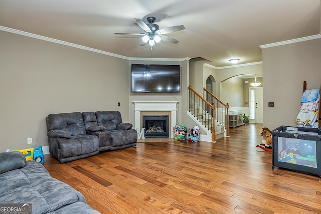 living area featuring arched walkways, a fireplace with flush hearth, wood finished floors, ornamental molding, and stairway