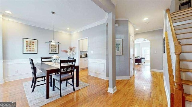 dining room featuring arched walkways, a decorative wall, stairway, light wood finished floors, and crown molding