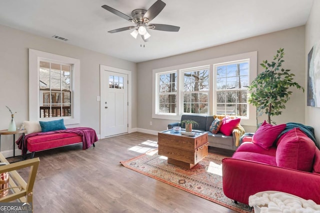 living room featuring visible vents, baseboards, wood finished floors, and a ceiling fan