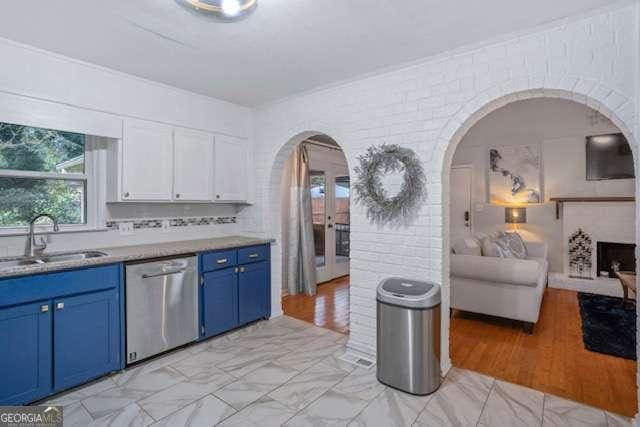 kitchen with arched walkways, blue cabinets, a sink, white cabinetry, and stainless steel dishwasher