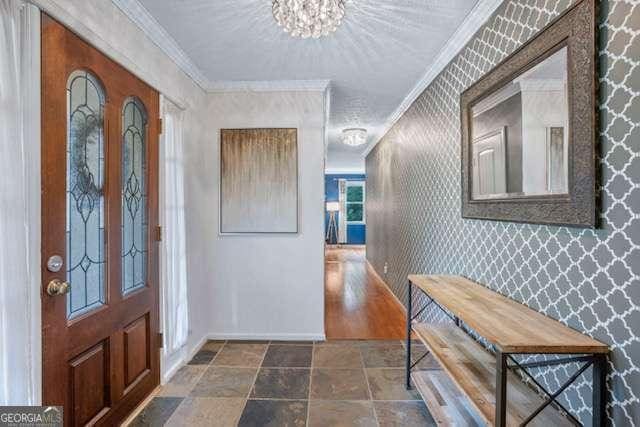 foyer entrance featuring an inviting chandelier, crown molding, baseboards, and wallpapered walls