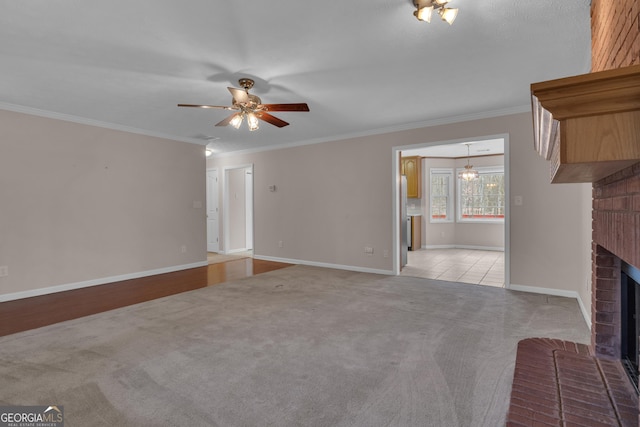 unfurnished living room featuring a brick fireplace, ceiling fan, crown molding, and light colored carpet