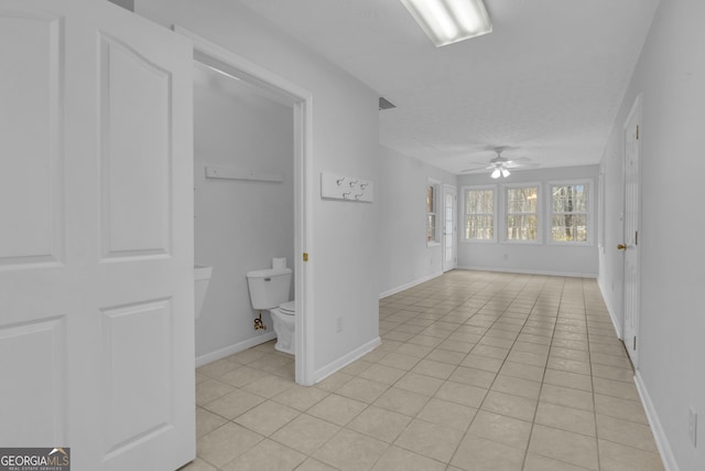 interior space with toilet, baseboards, a ceiling fan, and tile patterned floors