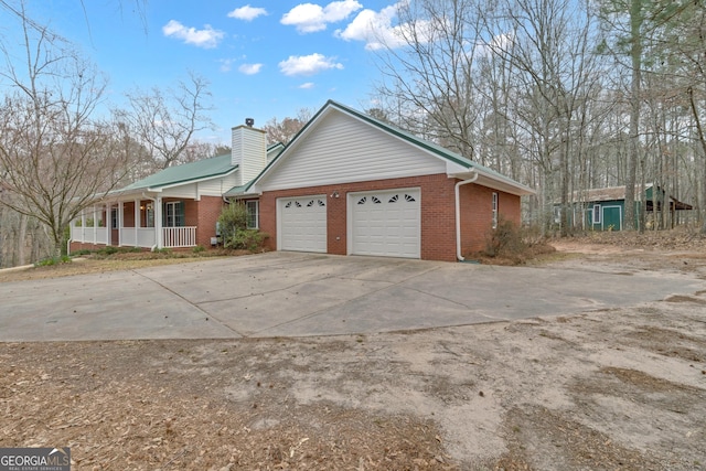 exterior space featuring driveway, a chimney, an attached garage, a porch, and brick siding