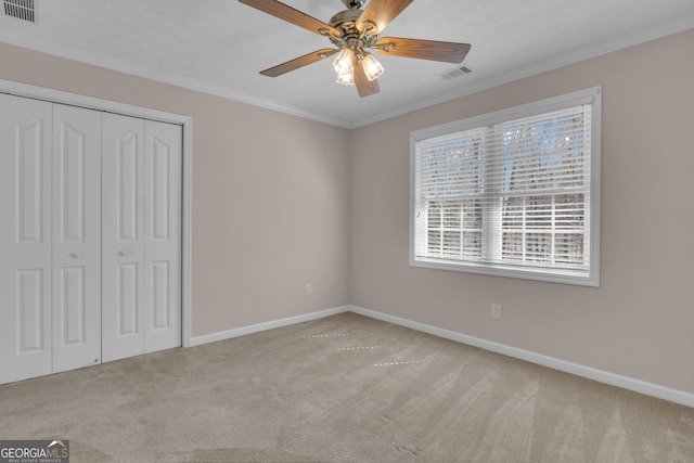 unfurnished bedroom featuring carpet flooring, visible vents, baseboards, a closet, and crown molding