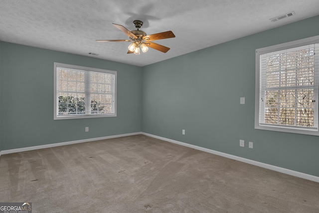 carpeted empty room with a textured ceiling, ceiling fan, visible vents, and baseboards