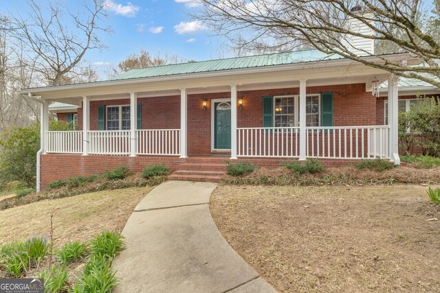 single story home with covered porch, metal roof, and brick siding