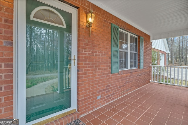 property entrance with a porch and brick siding