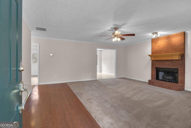 unfurnished living room with crown molding, a fireplace, visible vents, ceiling fan, and baseboards