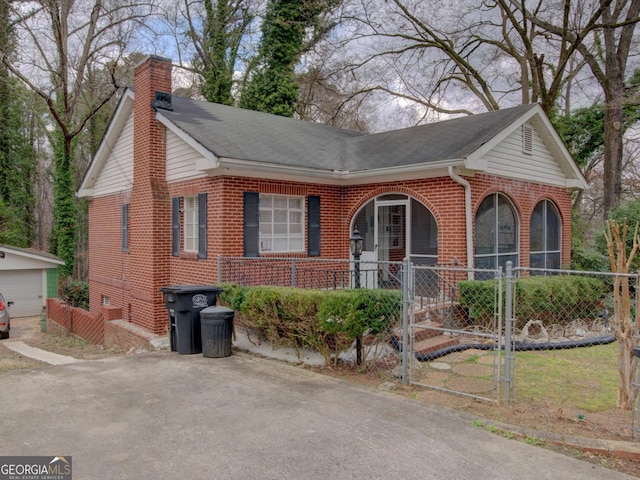 single story home featuring a fenced front yard, brick siding, roof with shingles, a chimney, and a gate