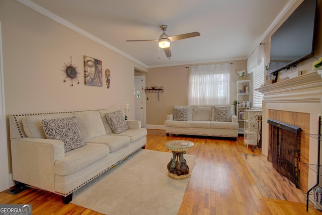 living room featuring a ceiling fan, a fireplace, ornamental molding, and wood finished floors