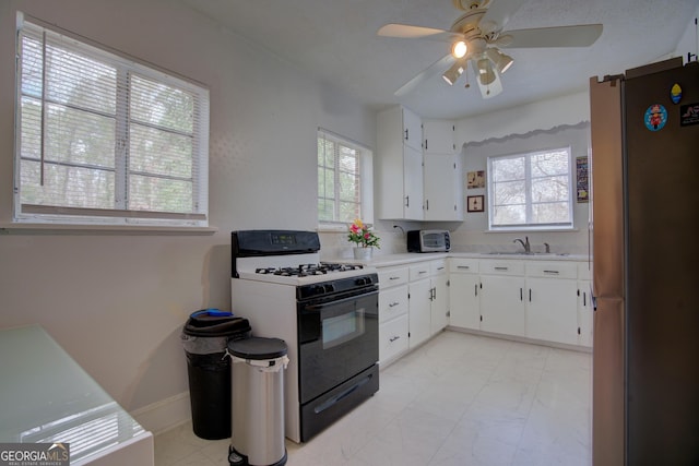 kitchen with light countertops, gas range oven, freestanding refrigerator, and white cabinetry