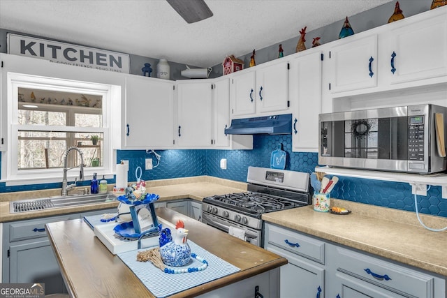 kitchen with backsplash, stainless steel appliances, a textured ceiling, under cabinet range hood, and a sink