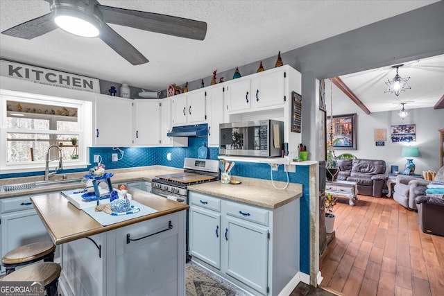 kitchen with under cabinet range hood, stainless steel appliances, open floor plan, tasteful backsplash, and a kitchen bar