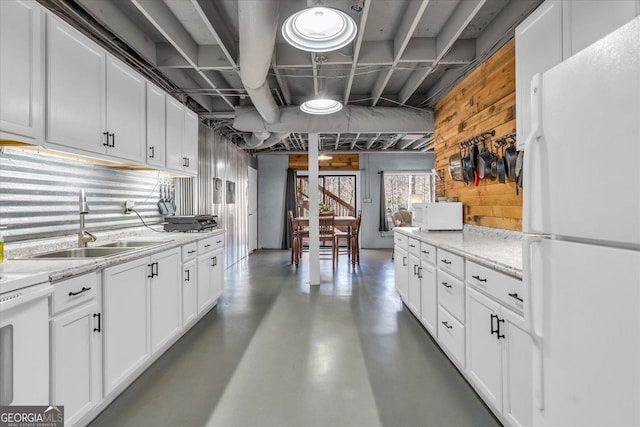 kitchen with concrete flooring, white appliances, wood walls, a sink, and white cabinetry