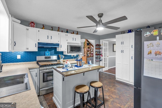 kitchen featuring under cabinet range hood, white cabinetry, light countertops, appliances with stainless steel finishes, and backsplash