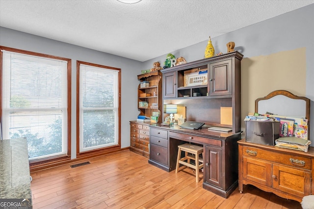 office space with a wealth of natural light, visible vents, light wood-style flooring, and a textured ceiling