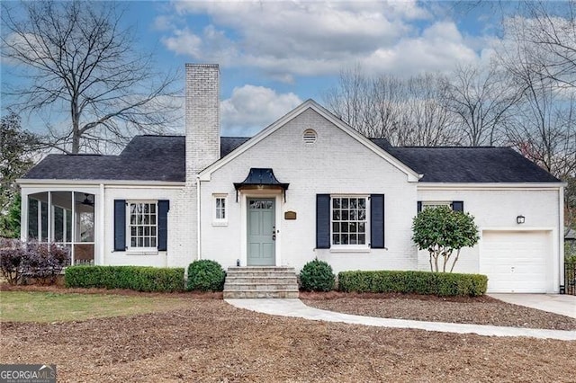 view of front facade with driveway, a garage, a sunroom, a chimney, and brick siding