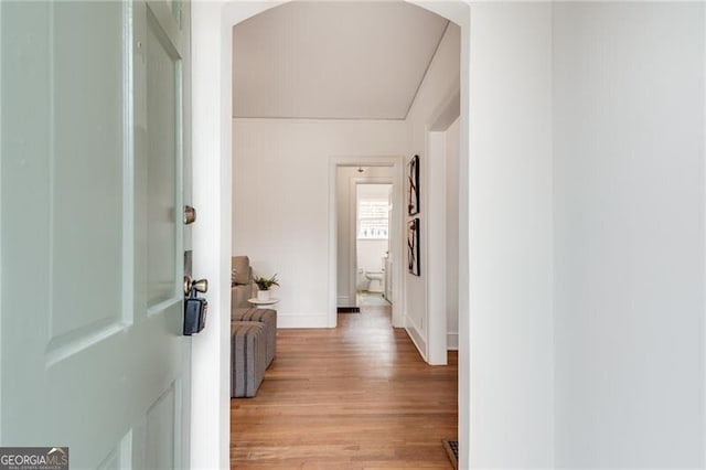 hallway featuring light wood-style floors, arched walkways, and baseboards