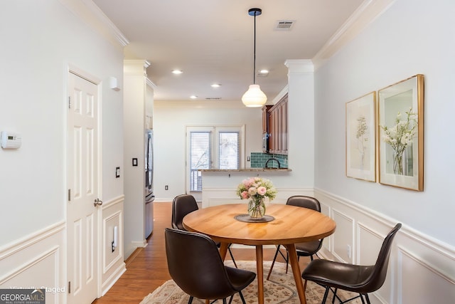 dining space with a decorative wall, a wainscoted wall, visible vents, light wood-style floors, and crown molding